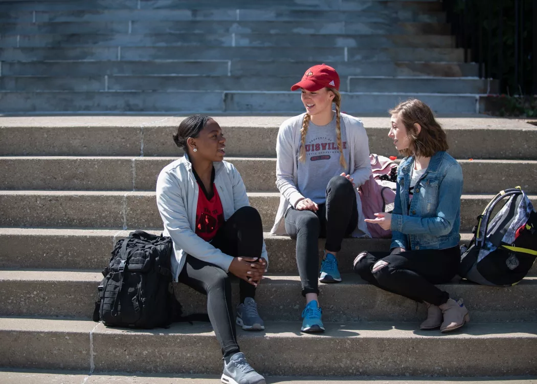 Three students hang out on steps of an academic building